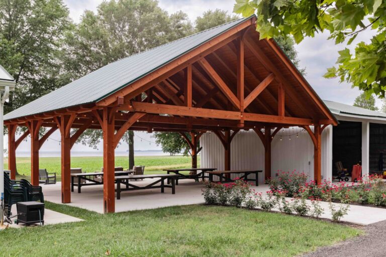 38x30 Kingston Pro Timber Frame Pavilion. Between barn and building. Lake in the distance.