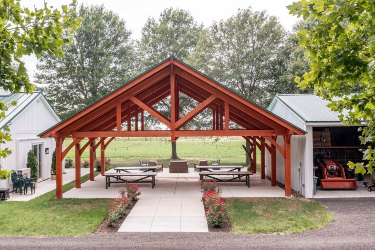 View of front of 38x30 Kingston Pro Timber Frame Pavilion. Wooden structure between two white buildings.