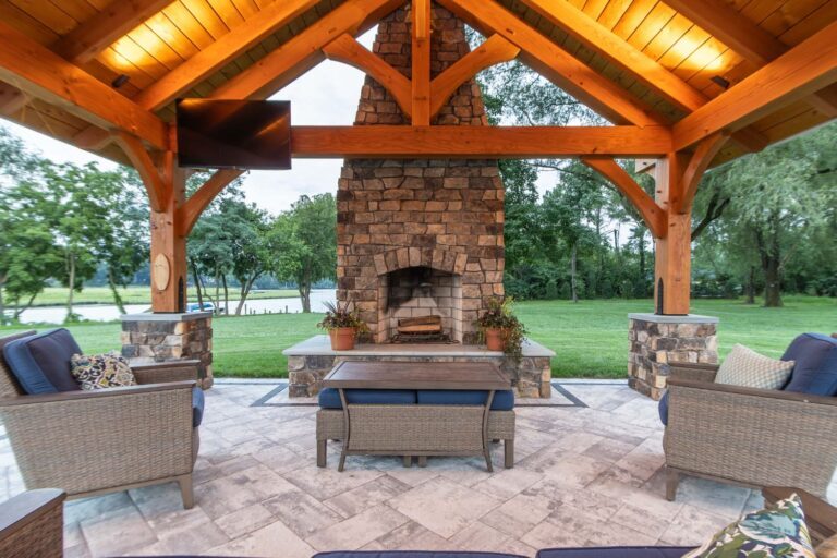 Interior view of pavilion lighting over a seating area in front of a built-in stone fireplace-visible lawn and trees in distance