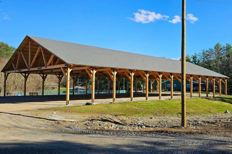 Outside of completed 70x140 Kingston Timber Frame Pavilion in Copake NY. Gravel road leads to pavilion, green grass in foreground with brilliant blue sky behind the pavilion