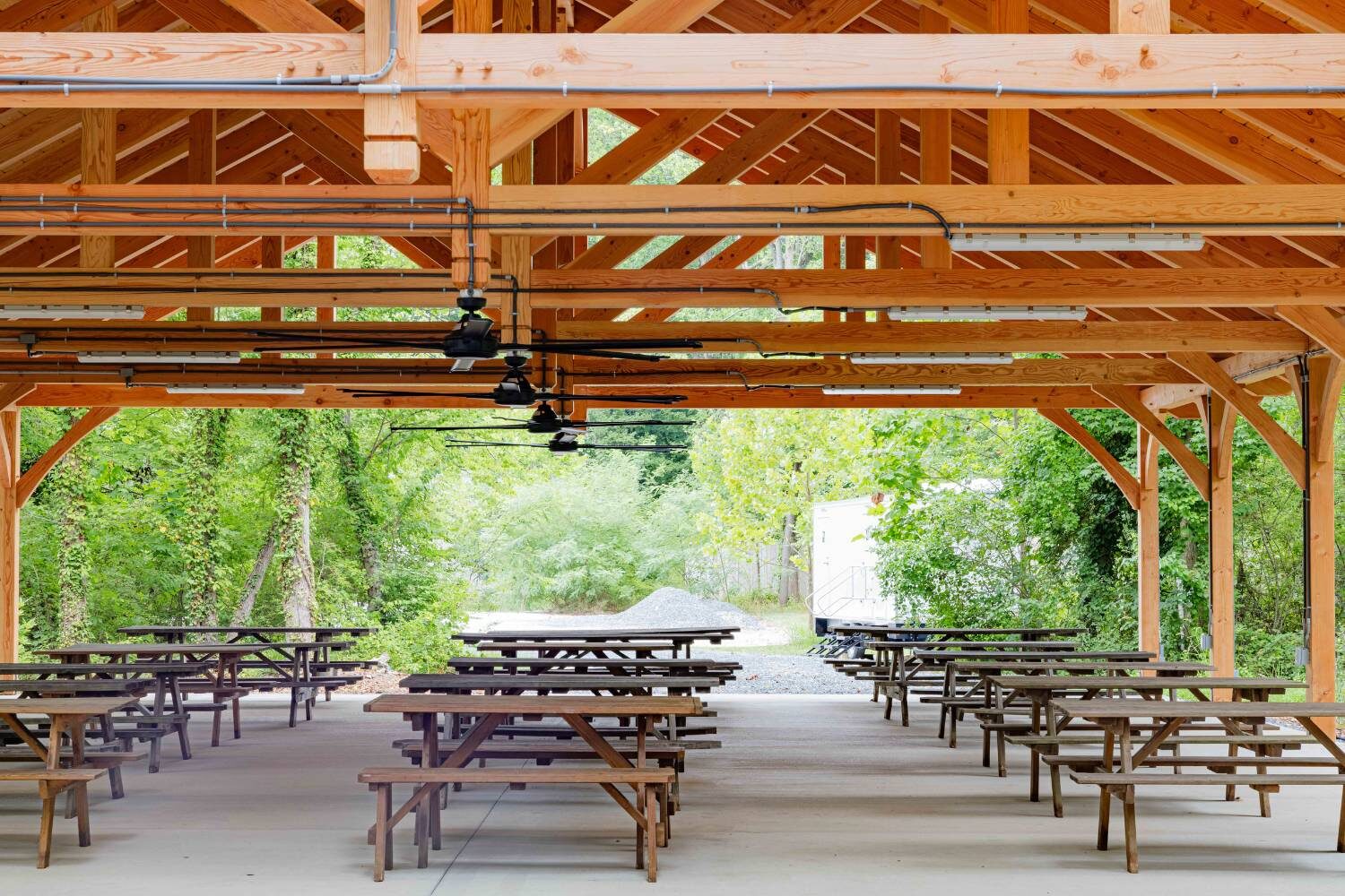 Underneath timber frame pavilion in the woods with picnic benches and fans